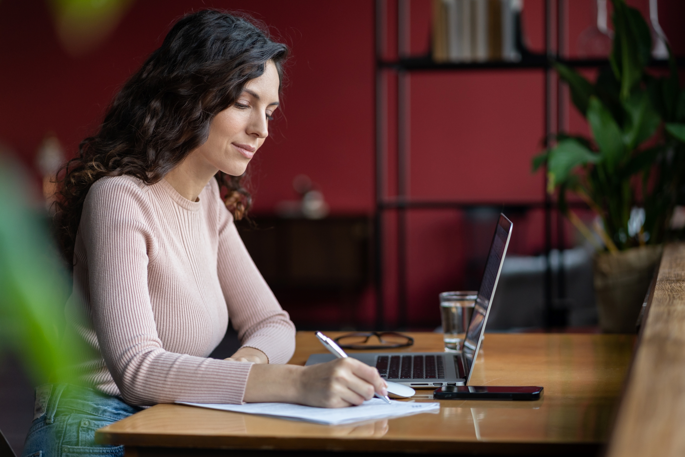 Woman writing on paper while looking at a laptop.